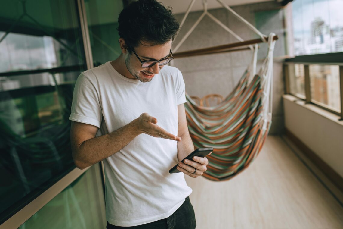 młody mężczyzna korzysta z telefonu stojąc na balkonie swojego mieszkania